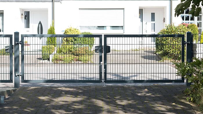 A Dobbeltlåge "TREND" komplet med Locinox låsekasse står lukket foran en bolig med hvide vægge, vinduer og buske i baggrunden.