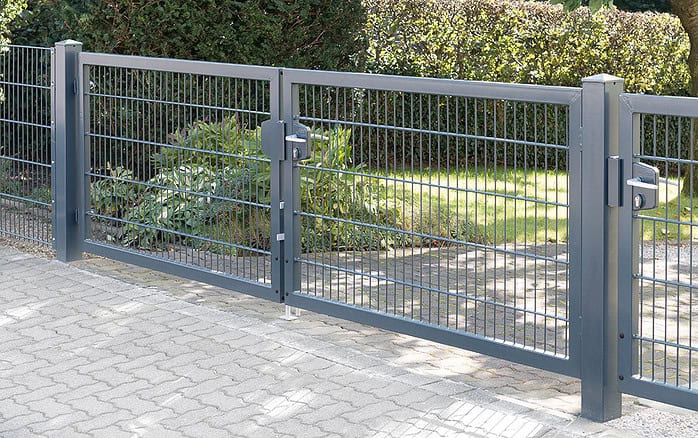 Dobbeltlåge "TREND" komplet med Locinox låsekasse, malet mørkegrå med lodrette og vandrette bjælker, står på en asfalteret gangbro og omslutter en grøn have med klippede buske og græs.