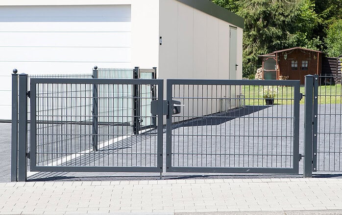 En Dobbeltlåge "TREND" Komplet med Locinox låsekasse står foran en asfalteret indkørsel, der fører til en hvid garage, med et lille skur og grønne områder i baggrunden.