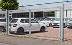 Flere hvide biler er parkeret på en indhegnet plads uden for en moderne industribygning, og en Dobbeltlåge "TREND" komplet med Locinox låsekasse er synlig nær fortovet og træet i forgrunden.
