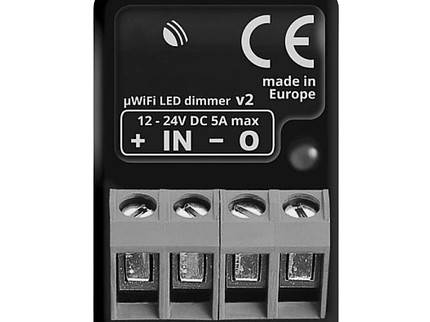 Nærbillede af en sort rektangulær enhed mærket "WLAN-modul til LED-hegnsbelysning" med certificeringer inklusive CE-mærke og "made in Europe". Perfekt til din LED-hegnsbelysning, den har fire skrueterminaler mærket "+ IN - 0" og specifikationer "12-24V DC 5A max".