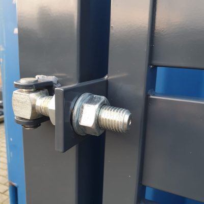 Nærbillede af en grå metalbolt og hængsel på en blå overflade, sandsynligvis en del af en portmekanisme som "Metallåge 2D Panelfyld 6/5/6mm Sort Ral 9005 Komplet", der lægger vægt på industrielt design og teknik.