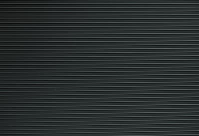Et nærbillede af en sort tekstureret Renovationsskjuler EcoHide Komplet-overflade med tynde vandrette riller jævnt fordelt henover. Rillerne skaber et lineært mønster, der tilføjer et subtilt element af dybde og detaljer til den ellers almindelige sorte baggrund.