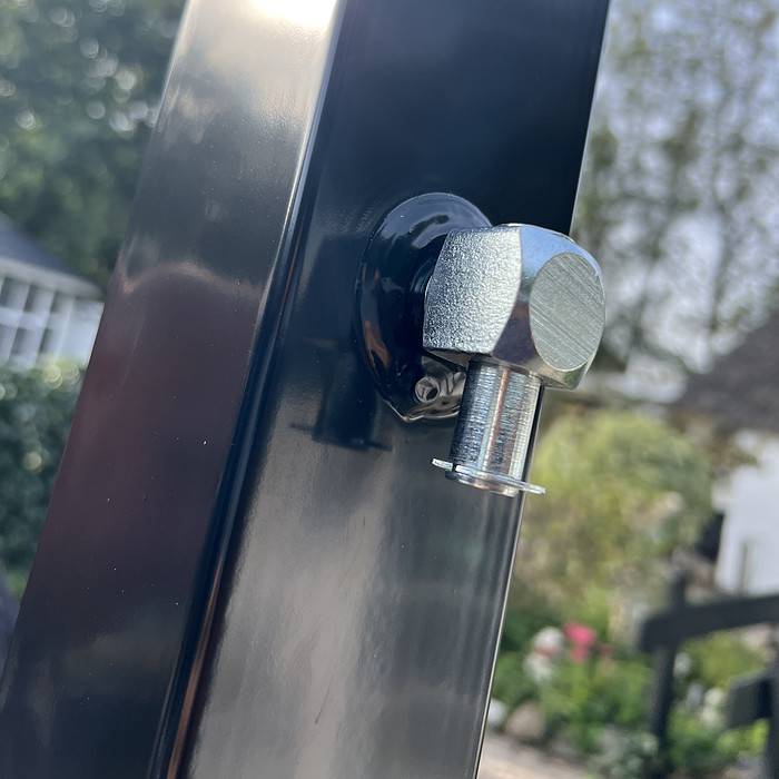 Nærbillede af en skinnende sekskantet bolt fastgjort til en sort metalstolpe, der matcher Metallåge 2D Panelfyld 6/5/6mm Sort Ral 9005 Komplet, med en udendørs haveindstilling sløret i baggrunden. Bolten er placeret perfekt ved hjørnet af denne robuste Metallåge.