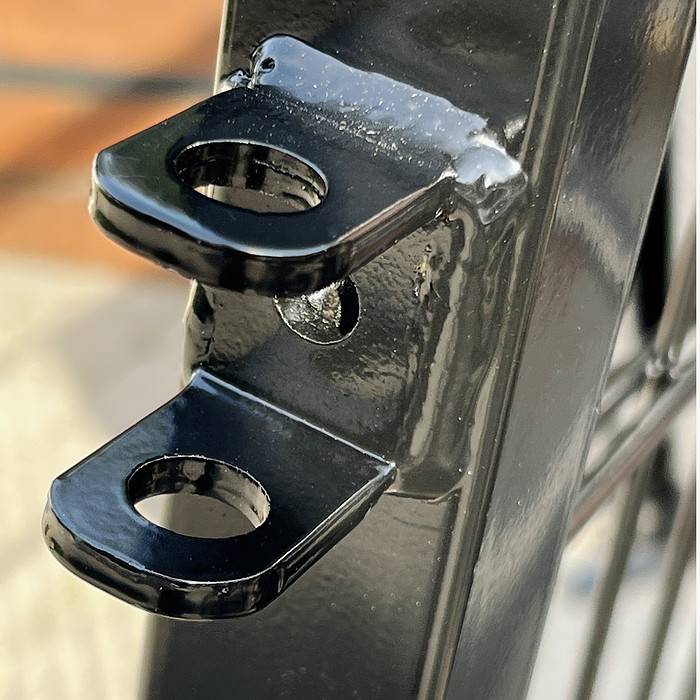 Nærbillede af et Metallåge 2D Panelfyld 6/5/6mm Sort Ral 9005 Komplet sort metalstykke med to vandrette, rektangulære faner, hver med et cirkulært hul i midten. Sort Ral 9005 metallågens skinnende overflade viser refleksioner. Sløret baggrund antyder udendørs omgivelser.