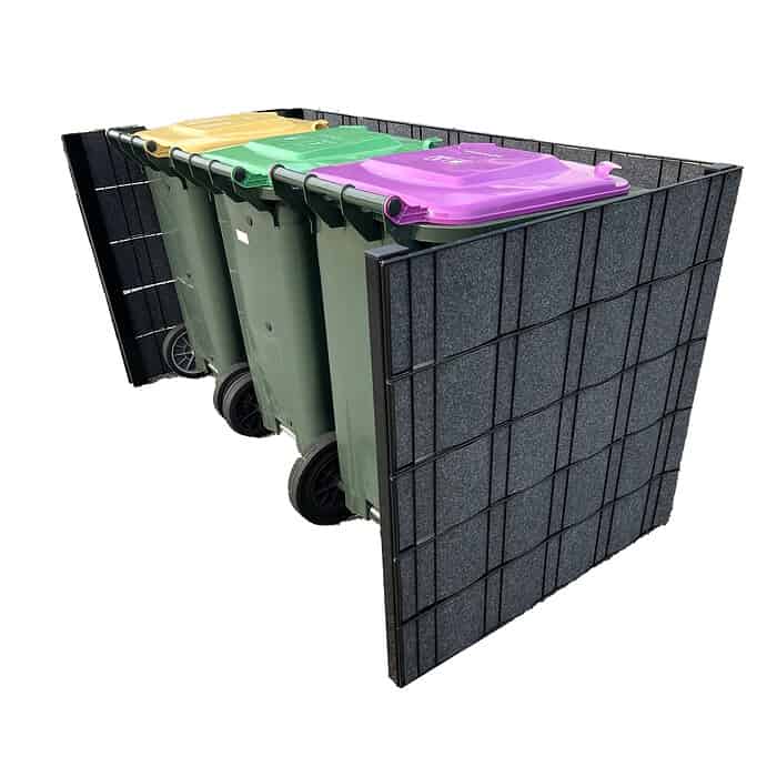 Tre grønne skraldespande på hjul med farvede låg (gul, grøn og lilla) er placeret i en rektangulær, mørkfarvet, paneleret Renovationsskjuler EcoHide Komplet. Indhegningen omgiver skraldespandene på tre sider, hvilket skaber et pænt og organiseret affaldsplads.