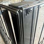 Nærbillede af et sort metalporthængsel med en låsemekanisme. Lågen og hængslet ser ud til at være en del af en robust, svejset struktur med synlige bolte. Baggrunden er en industriel indstilling med et betongulv og metalstænger, perfekt til at bruge Renovationsskjuler EcoHide Komplet i dit skraldespandsskjuler DIY-projekt.