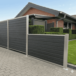 Et moderne hus med rødt murstensfacade og gråt skråtag er delvist omgivet af et højt, mørkegråt hegn med Stålstolpe med fodplade 80x80mm, som står på en asfalteret indkørsel.