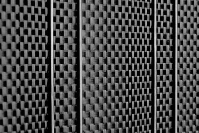 Et nærbillede af en tekstureret overflade med et gentaget mønster af små, hævede firkanter arrangeret i et gitter. Materialet ligner designet af Renovationsskjuler EcoHide Komplet og fremstår metallisk med et gråtonefarveskema, hvilket skaber en visuel effekt af dybde og dimension. Belysningen fremhæver teksturen.