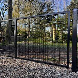 En dobbeltlåge 2D 6/5/6 mm sort RAL 9005 komplet inkl. stolper metalport med lodrette og vandrette stænger står på en grusindkørsel og åbner ud til en have med træer, græs og planter på en solskinsdag.