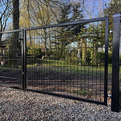 En dobbeltlåge 2D 6/5/6 mm sort RAL 9005 komplet inkl. stolper metalport med lodrette og vandrette stænger står på en grusindkørsel og åbner ud til en have med træer, græs og planter på en solskinsdag.