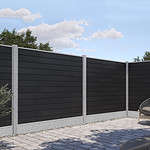 En baggård med sammenlåsende stenterrassegulve og moderne hegn. Komposit Hegn med galvaniseret bundplader, stålstolper & u-skinner – Type 2 er lavet af mørke vandrette paneler med lysegrå betonstolper og en grusplade i bunden. Der er nogle buske og træer i baggrunden, og en kurvestol er delvist synlig.