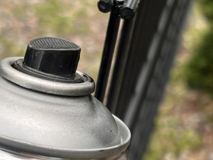 Et nærbillede af en Spraymaling Sort RAL 9005 400 ml spraymalingsdåse med en sort dyse, med et panelhøjde synligt i den slørede baggrund.