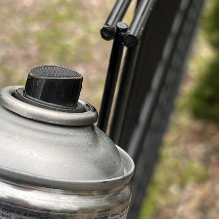 Et nærbillede af en Spraymaling Sort RAL 9005 400 ml spraymalingsdåse med en sort dyse, med et panelhøjde synligt i den slørede baggrund.