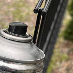 Et nærbillede af en Spraymaling Sort RAL 9005 400 ml spraymalingsdåse med en sort dyse, med et panelhøjde synligt i den slørede baggrund.