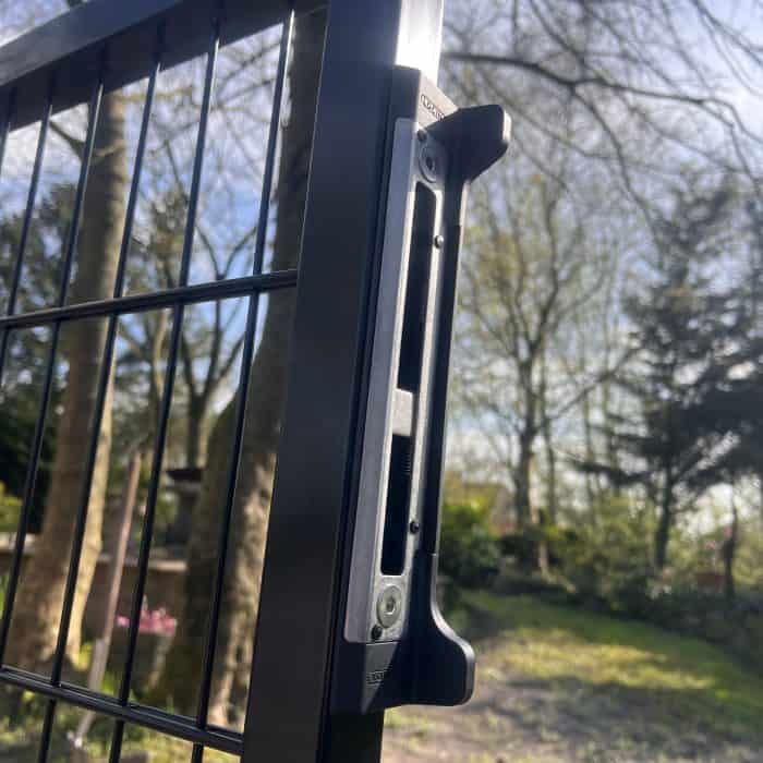 Nærbillede af en dobbeltlåge 2D 6/5/6 mm sort RAL 9005 komplet inkl. stolper portlås på et sort trådhegn med slørede træer og grønne områder i den solrige baggrund.