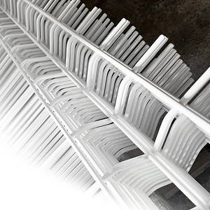 Nærbillede af stablede hvide metalrillede stativer, arrangeret på en overlappende måde, hvilket skaber et gentaget geometrisk mønster, der minder om Panelhegn 3D 5/5mm - HF PREMIUM Pulverlakeret Hvid RAL 9010. Billedet er taget fra et vinklet perspektiv, der viser symmetrien og tekstur af hvid metal hegn mod en sløret baggrund.