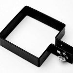 Lågestolpe Beslag Sort RAL 9005 (Designserie), et sort metalbeslag med kvadratisk form og 90 graders bøjning, er vist. Den har en bolt og møtrik på den ene side til fastgørelse eller fastgørelsesformål. Beslaget er placeret på en hvid baggrund.