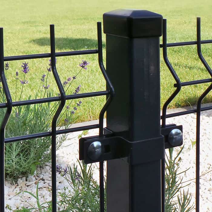 Nærbillede af et metal Hegn 3D panel "HF-DESIGN SERIE" i sort, med stålstolper og beslag, med bølgede trådnetpaneler fastgjort med bolte. Bag hegnet er grønt græs og blomstrende lavendelplanter delvist synlige sammen med små hvide sten på jorden.