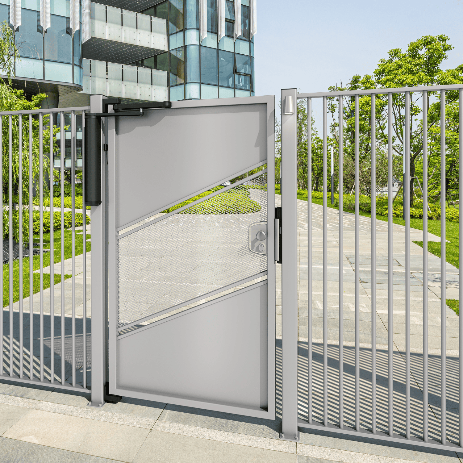 En moderne metalport med et geometrisk design og en Motoriseret og Automatiseret Portlukker til Fodgængerporte – VENUS er flankeret af et metalhegn. Porten er lidt åben og afslører en gangbro indeni. Træer og grønt græs er synlige i baggrunden sammen med en moderne glasbygning. Himlen er klar og solrig.