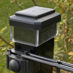 Et nærbillede af en Solcelledrevet LED-lampe fastgjort til hegnsstolper, med en gennemsigtig bundsektion. Placeret udendørs står den midt i levende grønt græs og delvist slørede planter og blander funktionalitet med naturen i et slankt 60x40 mm design.