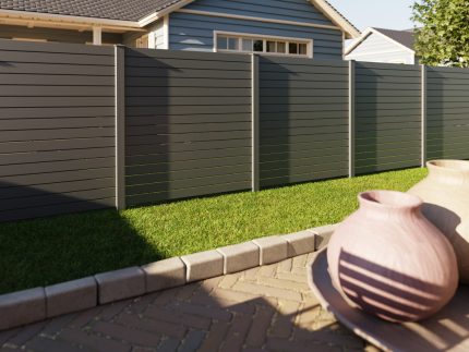 Vidual Pure – Jalousihegn i aluminium med rhombeprofil privatlivshegn står i en baghave med grønt græs, en brolæggerterrasse og vaser. Et lyseblåt hus med hvid trim er synligt bag det moderne grå aluminiumshegn.