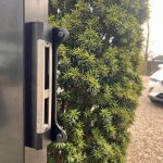 Nærbillede af en sort metalport med en Locinox-overflademonteret slutblik/anslag i rustfri stål til indstikslåse fastgjort til stolpen.