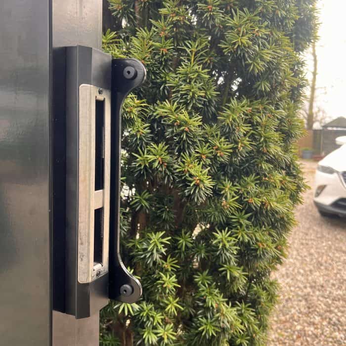 Nærbillede af en sort metalport med en Locinox-overflademonteret slutblik/anslag i rustfri stål til indstikslåse fastgjort til stolpen.