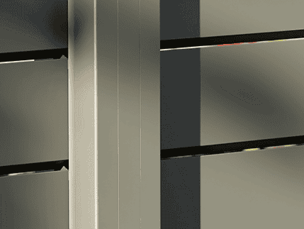 Nærbillede af Vidual Pure – Jalousihegn i aluminium med rhombeprofil i lysegrå, med vandrette lameller med sollys, der kaster skygger langs det moderne hegns overflade.