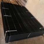 En stak 3D-panelhegn 4/4mm 173 cm SORT (125 m) + stolper 60×40 mm (240 cm) - Outlet-pakke-paneler er pænt organiseret med hvide lynlåse på et betongulv ved siden af en beige struktureret væg.