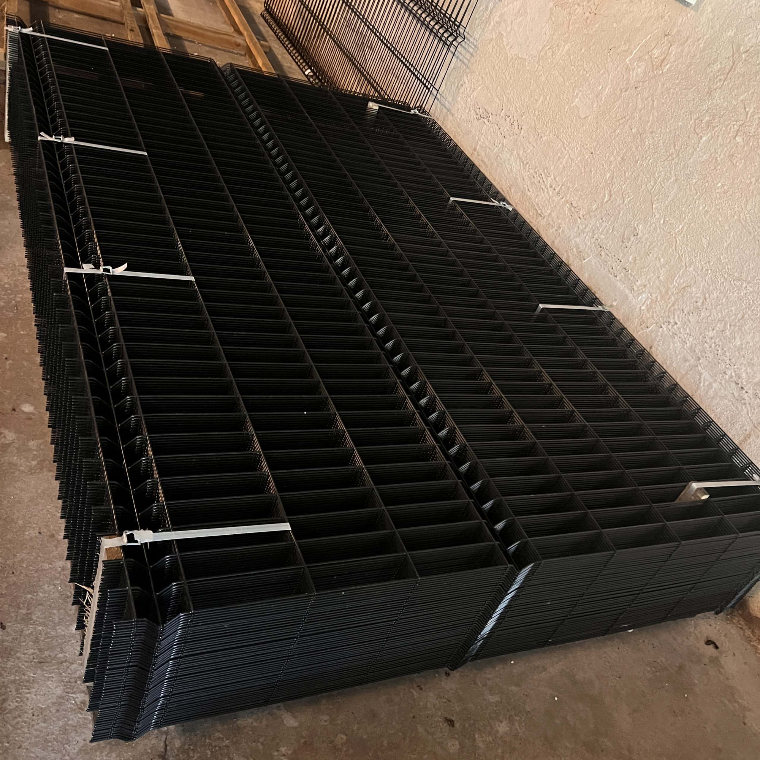 En stak 3D-panelhegn 4/4mm 173 cm SORT (125 m) + stolper 60×40 mm (240 cm) - Outlet-pakke-paneler er pænt organiseret med hvide lynlåse på et betongulv ved siden af en beige struktureret væg.