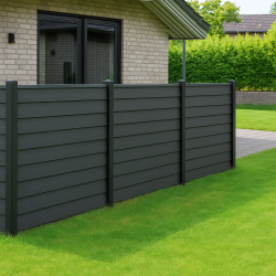 En moderne baghave med grønt græs, en asfalteret gangsti og træer har et elegant gråt privatlivshegn lavet af HF dobbeltklink kompositprofiler med træstruktur - 25 mm, ved siden af et beige murstenshus med store vinduer.