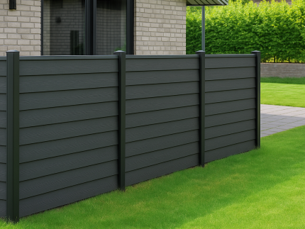 En moderne baghave med grønt græs, en asfalteret gangsti og træer har et elegant gråt privatlivshegn lavet af HF dobbeltklink kompositprofiler med træstruktur - 25 mm, ved siden af et beige murstenshus med store vinduer.