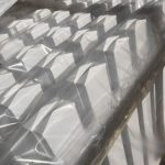 Stakke af hvid Outlet: Stakithegn i plast - Profexline 180x80 cm bue op er pakket ind i klar plast, og deres pyramideformede toppe kaster kantede skygger og mønstre i sollyset.