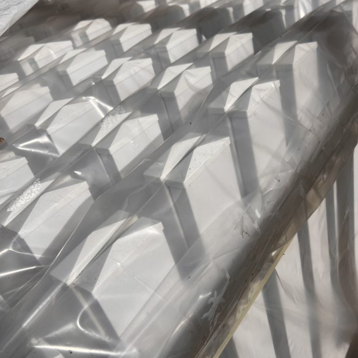 Stakke af hvid Outlet: Stakithegn i plast - Profexline 180x80 cm bue op er pakket ind i klar plast, og deres pyramideformede toppe kaster kantede skygger og mønstre i sollyset.