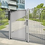 En moderne fodgængerport i metal med et geometrisk mønster står lukket, omgivet af lodrette stænger. Bag den fører en sti forbi grønne græsplæner og træer mod en moderne glasbygning under en klar himmel.