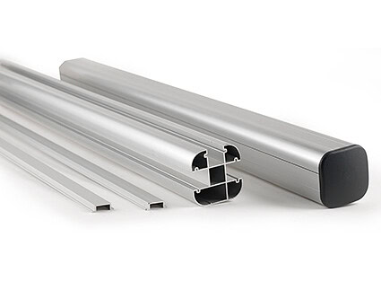 Fire ekstruderede aluminiumsprofiler, herunder én med en sort plastendekappe, er anbragt på en hvid baggrund. Profilerne har forskellige tværsnitsformer og -størrelser.