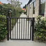 Låge på mål med lodret balusterfyld (Baluster P-20) i specialfarven RAL 8019 gråbrun, monteret mellem to lågestolper ved havegangen – kundefoto