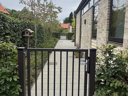 Låge på mål med lodret balusterfyld (Baluster P-20) i specialfarven RAL 8019 gråbrun, monteret mellem to lågestolper ved havegangen – kundefoto
