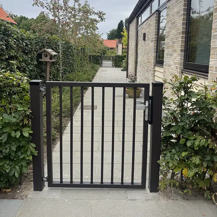 Låge på mål med lodret balusterfyld (Baluster P-20) i specialfarven RAL 8019 gråbrun, monteret mellem to lågestolper ved havegangen – kundefoto