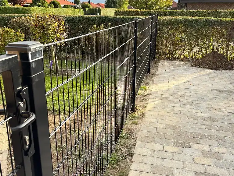 Sort 2D-panelhegn langs en flisegang