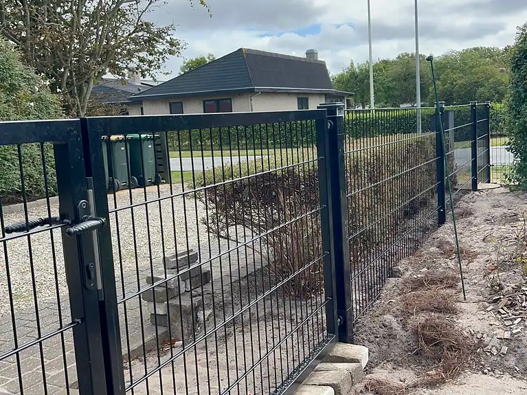 Sort 2D-panelhegn med låge langs indkørslen