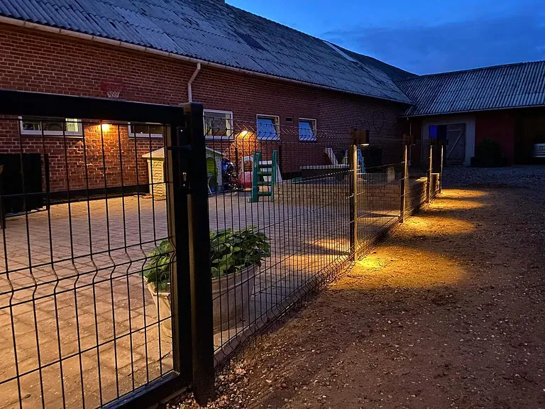 3D-panelhegn med varmt lys langs gårdspladsen i skumringen
