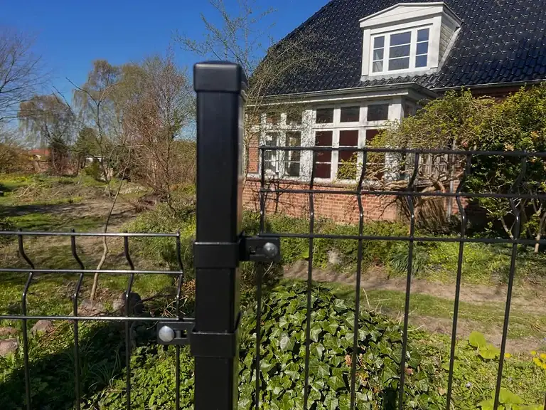 Sort 3D-panelhegn med designbeslag foran en rød murstensbygning