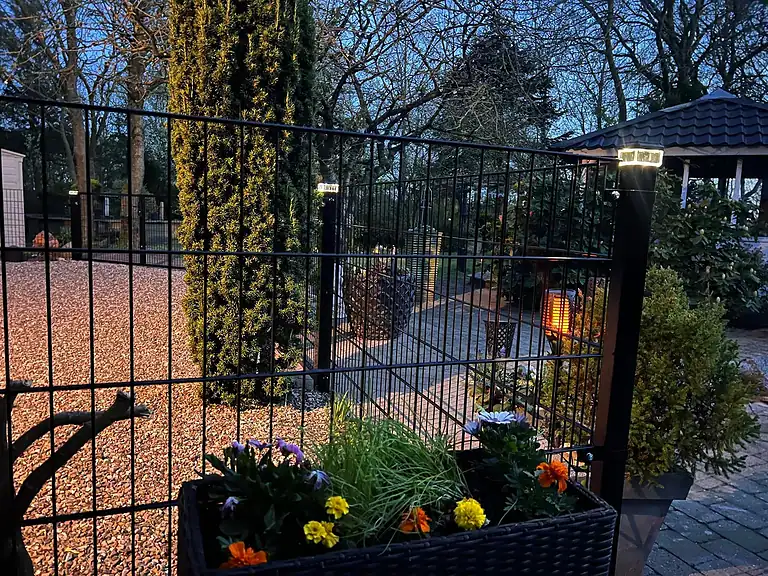 Sort panelhegn med blomsterkasse og lys i stolperne om aftenen