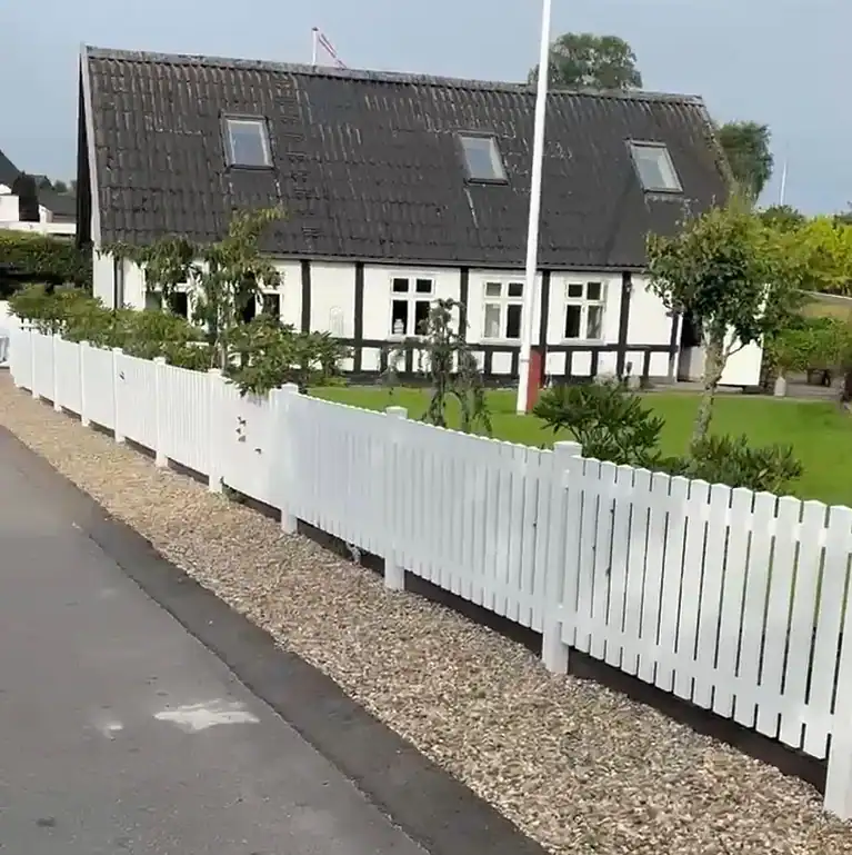 Hvidt stakit langs vejen foran et hvidt bindingsværkshus