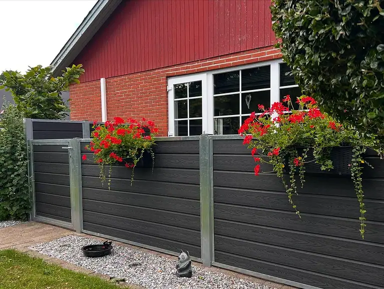 Komposithegn med blomsterkasser foran et rødt træhus