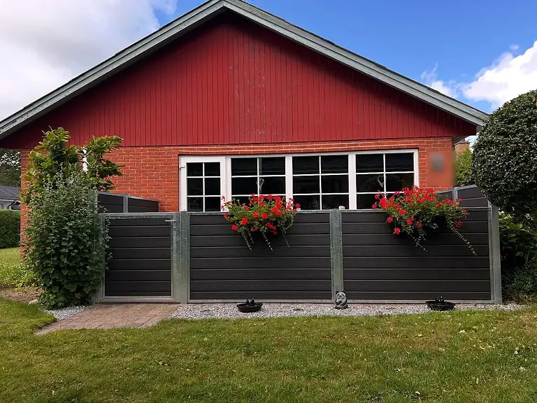 Komposithegn med varmgalvaniserede stolper og blomsterkasser foran et rødt træhus