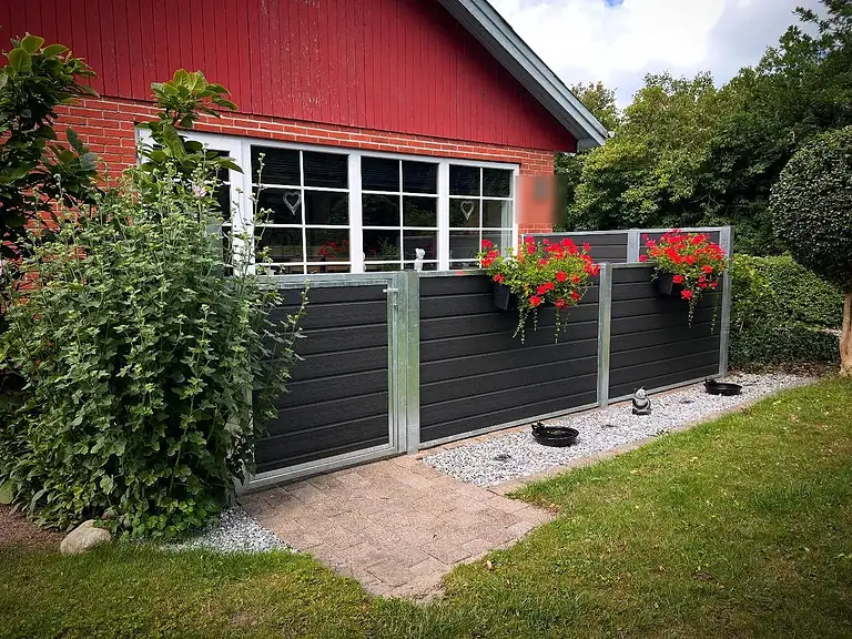 Lavt komposithegn med blomsterkasser langs et rødt hus