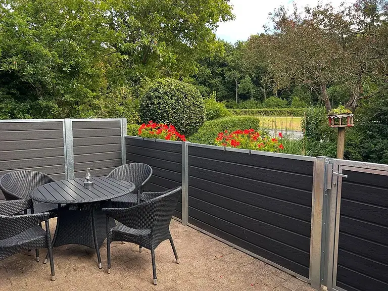 Komposithegn om en terrasse med havebord og stole